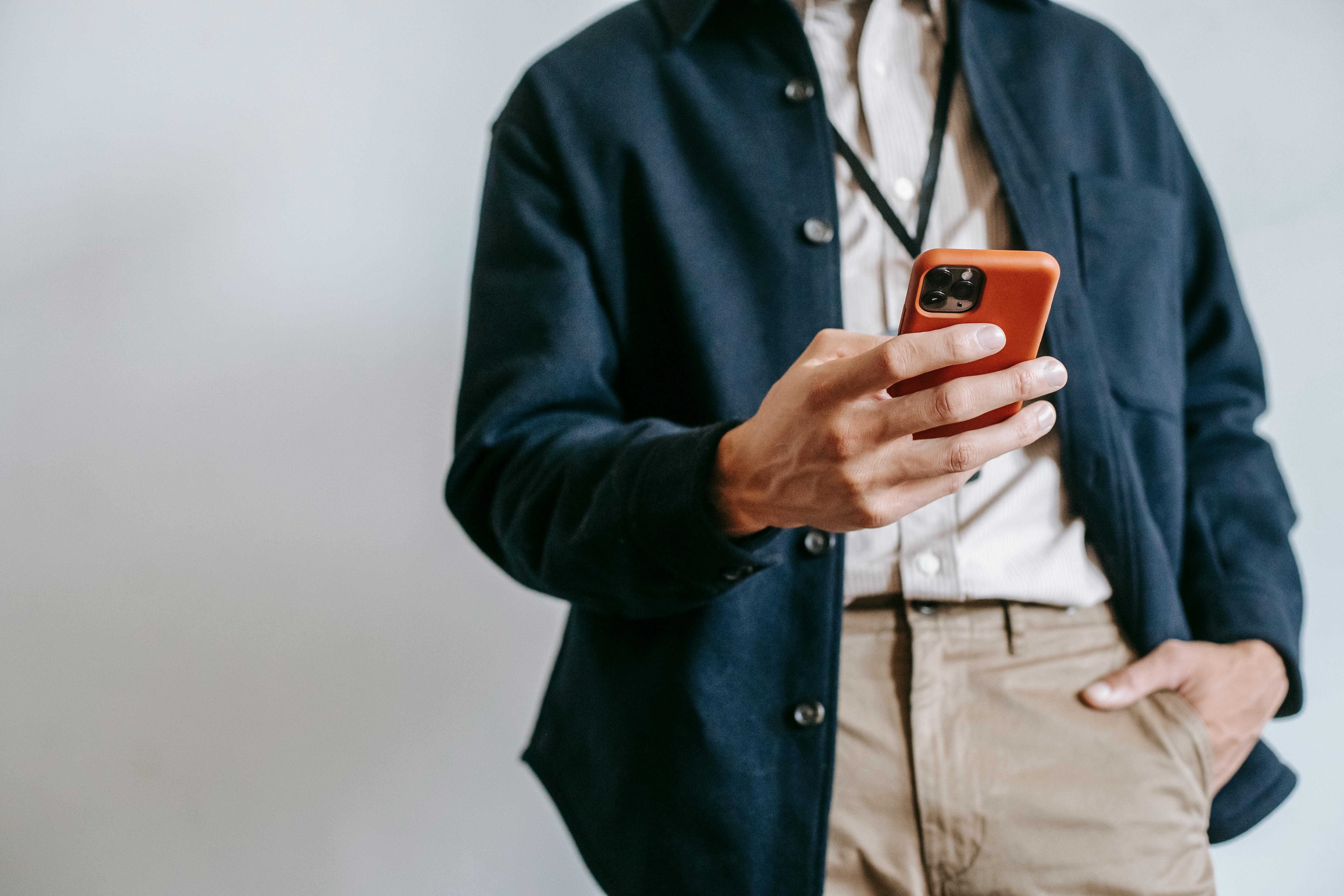 A man in casual attire browsing on a smartphone indoors, showcasing modern tech lifestyle.